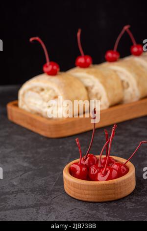 Nachtisch-Meringue-Rolle mit frischer Birne, dekoriert mit Kirsche auf dunklem Hintergrund in einem Café. Speicherplatz kopieren Stockfoto