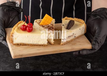 Klassischer Käsekuchen mit Kirschen, Schokolade und Keksen auf einem Tablett auf dunklem Hintergrund Stockfoto