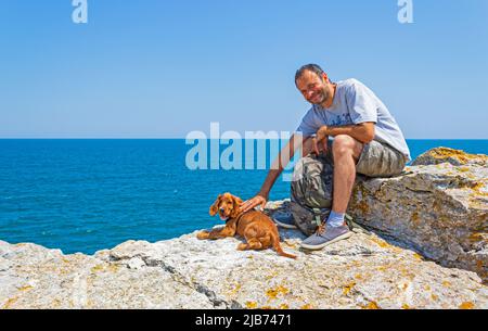 Niedliche vier Monate alten männlichen englischen Welpen Cocker Spaniel stehen mit einem Mann auf einem felsigen Strand an schönen Sommertag Tyulenovo Dorf Bulgarien Stockfoto