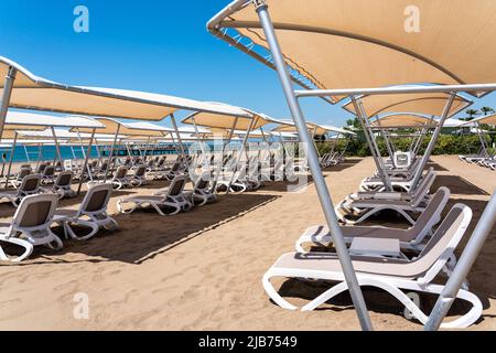 Eine Reihe von Sonnenliegen an einem einsamen Sandstrand im türkischen Resort. Sonnenliegen warten in einem Hotel auf Touristen Stockfoto