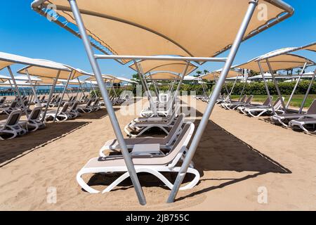 Eine Reihe von Sonnenliegen an einem einsamen Sandstrand im türkischen Resort. Sonnenliegen warten in einem Hotel auf Touristen Stockfoto