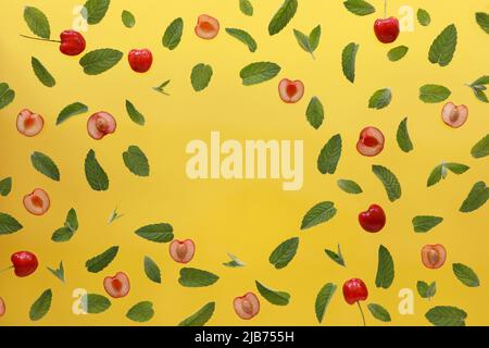 Sommerhintergrund, Rahmen mit frischen Kirschfrüchten und Minze auf gelbem Hintergrund. Flach liegend. Sommerliches Obst-Konzept. Stockfoto