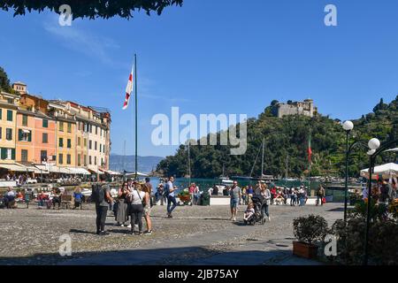 Blick auf den berühmten Hauptplatz von Portofino, genannt 'Piazzetta', mit Touristen und das braune Schloss auf dem Vorgebirge im Frühling, Genua, Ligurien Stockfoto