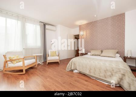 Schlafzimmer mit Doppelbett, Schaukelstühlen aus Holz, hellem Holzboden und großem Fenster mit Vorhängen Stockfoto