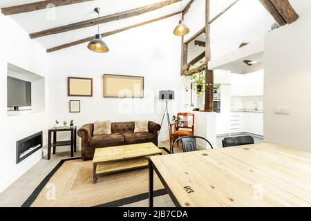 Wohnzimmer der Penthouse-Wohnung mit hohen Decken, renovierten Vintage-Holzbalken, chesterfield Sofa und industriellen Holztischen Stockfoto