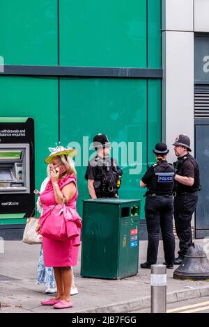 Epson Surrey, London, Großbritannien, Juni 03 2022, Frau in pinkfarbenem Kleid mit Mobiltelefon und Polizeibeamten im Hintergrund Stockfoto