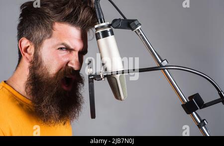 Studio-Aufzeichnungen. Bärtiger Mann, der im Kondensatormikrofon singt. Professioneller Sänger. Karaoke-Sänger. Stockfoto