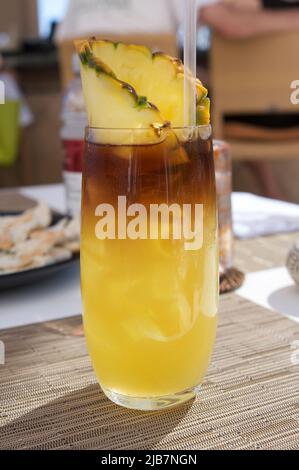 Ein Mai Tai Cocktail mit einem Stück Ananas in einem hohen klaren Glas an einer tropischen Bar an einem sonnigen Tag. Stockfoto