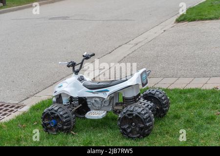 Ein Kinder-ATV aus Kunststoff, das von Kindern auf dem grünen Gras am Straßenrand hinterlassen wurde Stockfoto