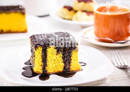 Ein Stück Karottenkuchen mit cremigem Schokoladenfrosting, serviert mit Kaffee mit Milch, typisch für brasilianische Juni-Feste, hausgemachter Kuchen Stockfoto