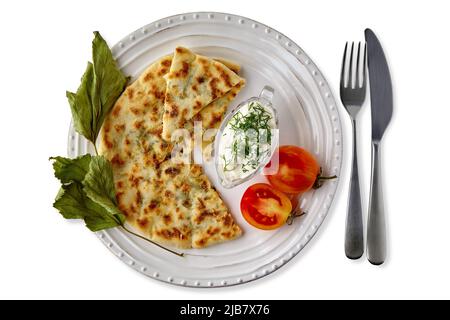 Fladenbrote mit Käse und Kräutern und Joghurtsauce auf einem weißen Teller mit Besteck dekoriert mit Tomaten und getrockneten Johannisbeerblättern. Vegetarische Gerichte Stockfoto