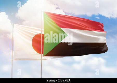 Sonniger blauer Himmel und Flaggen des sudan und japans Stockfoto