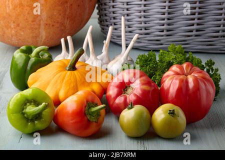 Reifes Gemüse und Gemüse aus dem Garten auf einem blauen Holztisch vor dem Hintergrund eines Korbes und Kürbis Stockfoto