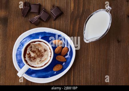 Tasse Cappuccino-Mandeln, Schokolade und Milch in einem Milchkännchen aus Glas auf einem dunklen Holztisch Stockfoto