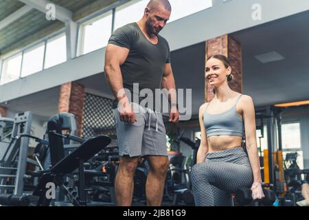 Ein schönes, athletisches Mädchen unter der Aufsicht eines Trainers macht Beinübungen mit Hanteln unter , Erhöhung der Muskelmasse . Hochwertige Fotos Stockfoto