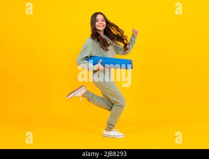 Mädchen Teenager im Trainingsanzug. Fröhliches, niedliches Kind in einem gelben Sportanzug auf gelbem Hintergrund. Laufen und springen. Sportbekleidung Werbekonzept. Stockfoto