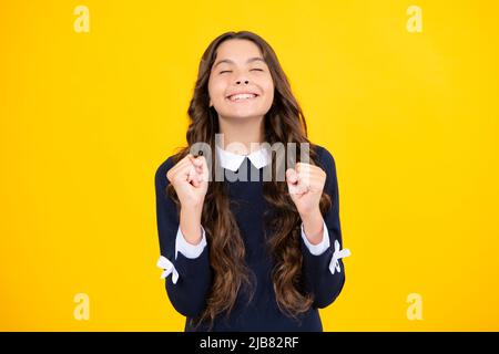 Froh Teenager-Mädchen kreuzt die Finger, schließt die Augen mit Vergnügen, erwarten hören gute Nachrichten, isolierten gelben Hintergrund. Glückliches Kind freut sich, dass seine Stockfoto