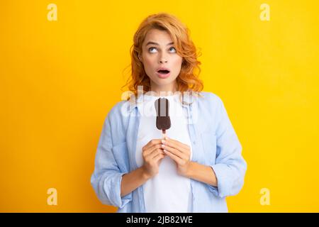 Portrait von fröhlichen lustigen Teenager-Mädchen genießt den Verzehr von kalten gefrorenen Dessert, isst köstliche Schokolade Eis, gelber Hintergrund. Überrascht überrascht Stockfoto