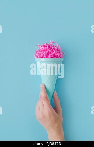 Frau Hand halten rosa Papier Eis Schaufel mit Eis Kunststoff-Kegel auf hellblauem Hintergrund. Minimales Sommerkonzept. Mikroplastik in Lebensmitteln Stockfoto