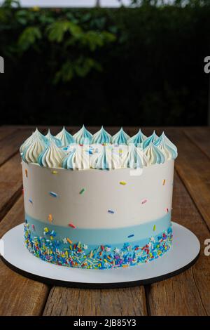 Vanillekuchen mit Buttercreme-Zuckerguss, verziert mit bunten Streuseln. Garten im Hintergrund vertikal. Stockfoto