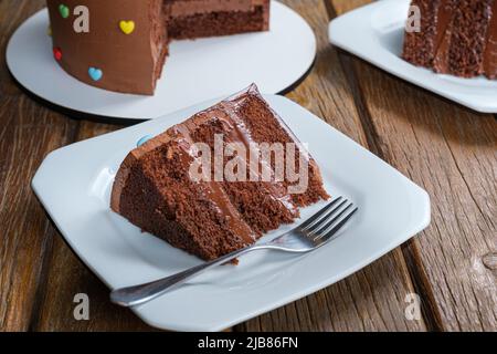 Scheibe Schokoladenkuchen mit Füllung und halbsüßen Schokoladen-Ganache-Zuckerguss. Stockfoto
