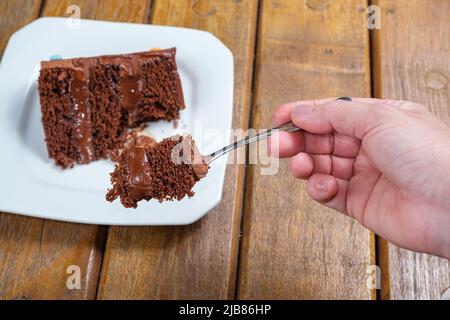 Frau zeigt ein Stück Schokoladenkuchen mit einer halbsüßen Ganache-Füllung aus Schokolade. Stockfoto