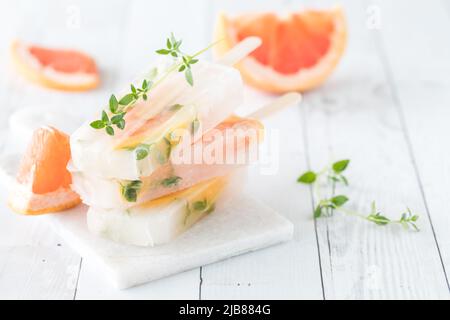 Ein kleiner Stapel Grapefruit-Thymian-Eiszapfen auf einem weißen Schiefertisch aus Holz. Stockfoto