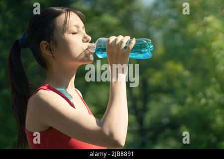 Schöne junge Frau joggt morgens im Park und trinkt blaue Isotone aus einer Flasche. Stockfoto