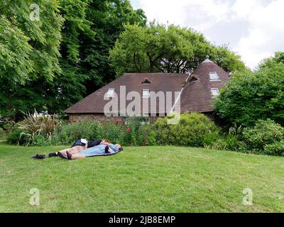 London, Greater London, England, Mai 28 2022: Menschen, die auf dem Rasen neben dem Cottage im Holland Park in der Gegend von Kensington schlafen. Stockfoto