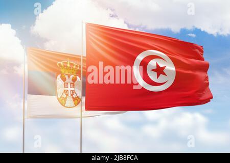 Sonniger blauer Himmel und Flaggen von tunesien und serbien Stockfoto
