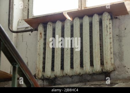 Eine alte rostige gusseiserne Batterie hob die Fenster am Eingang eines mehrstöckigen Gebäudes in der Ukraine an, heizte das Haus, die Batterie im Haus i Stockfoto