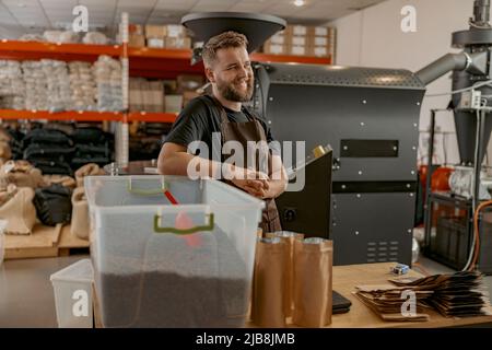 Porträt eines lächelnden Geschäftsbesitzers auf dem Hintergrund einer eigenen kleinen Kaffeefabrik, die wegschaut Stockfoto