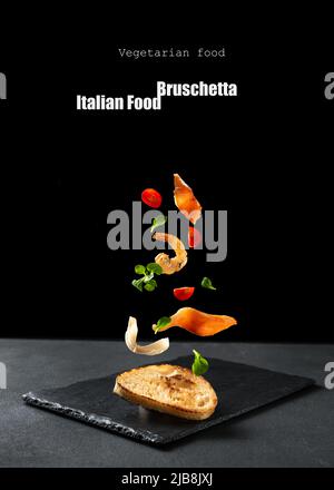 Italienische Vorspeise auf schwarzem Hintergrund. Bruschetta-Zutaten für die Vorspeise, die auf schwarzem Hintergrund fliegen. Sandwich auf schwarzem Hintergrund mit salm Stockfoto