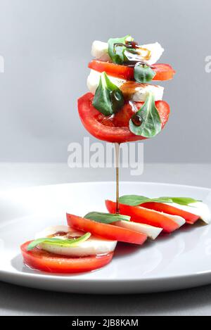 Italienischer Caprese-Salat mit geschnittenen Tomaten, Mozzarella, Basilikum, Olivenöl auf grauem Hintergrund. Fliegende Inridients. Italienischer Salat auf schwarzem Teller mit Stockfoto
