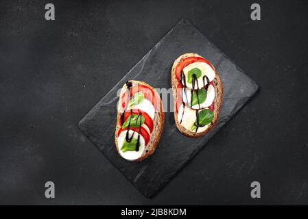 Offene Sandwiches mit einem in Scheiben geschnittenen Sauerteigbrot-Sandwich mit Kirschtomaten, Mini-Mozzarella, frischem Basilikum, Olivenöl und Oregano in der Mitte Stockfoto