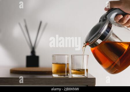 Heißer Tee wird in Glas-Teetasse gegossen. Gieße den heißen Tee in die Teetasse. Es gab weiches Sonnenlicht, das in eine warme Atmosphäre schien. Stockfoto