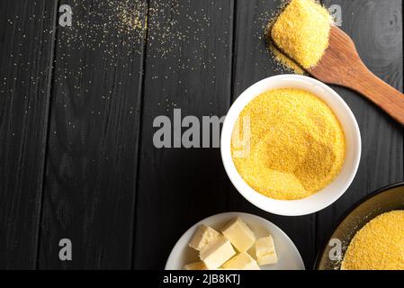 Polenta- oder Maismehl-Mehl. Gemahlene getrocknete Mais- oder Maiskörner in einer weißen Schüssel und Holzlöffel in Nahaufnahme auf weißem Hintergrund. Speicherplatz kopieren Stockfoto