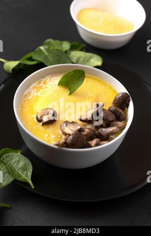Frühstücksbrei mit Pilzen. Polenta ist ein traditionelles norditalienisches Gericht aus grobem Maismehl. Vertikaler Rahmen Stockfoto