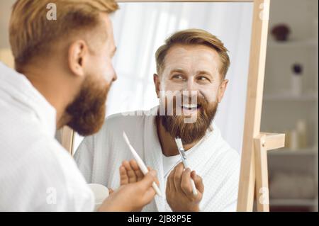 Nahaufnahme von lustigen Mann im Spiegel reflektiert, der kosmetische Maske für die Gesichtspflege anwendet. Stockfoto