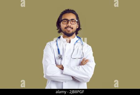 Porträt eines jungen indischen Arztes im weißen Mantel mit Stethoskop, das mit gefalteten Armen steht Stockfoto