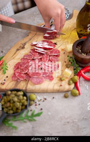 Frau schneidet spanische Wurst-Fuet-Salami mit Messer auf einer Hausküche Stockfoto