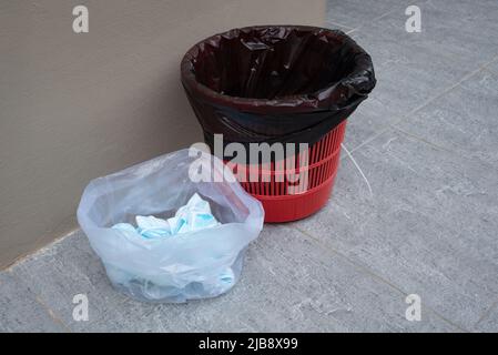 Gesichtsmasken in Plastiktüte vom allgemeinen Müll in schwarzem Behälter getrennt. Stockfoto