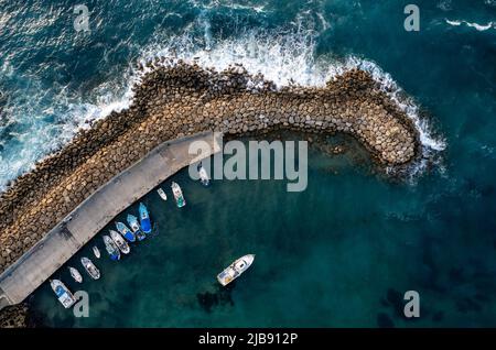 Luftdrohnenansicht der Fischerboote, die am Hafen bei Wellenbrecher festgemacht sind. Stürmische Wellen auf See Stockfoto