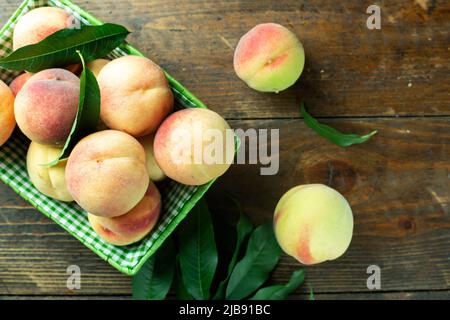 Reife Pfirsiche im Korb auf Holzhintergrund. Hausernte aus dem eigenen Garten. Gesunde Ernährung. Stockfoto