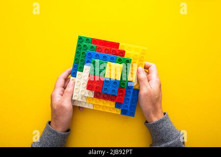 Hand, die einen weißen Spielzeugstein auf bunte Plastikbausteine legt und so eine Struktur erschafft Stockfoto