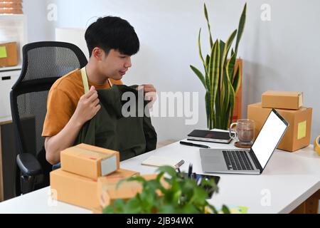 Start-up-Unternehmer Kleinunternehmen zeigen Kleidung vor dem Laptop, während die Aufzeichnung vlog Video und Live-Streaming online. Stockfoto