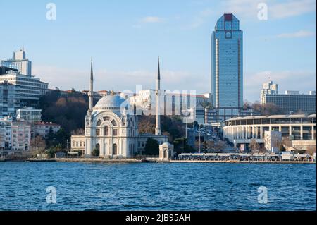 ISTANBUL, TÜRKEI - Januar 2022: Blick von Bosforus auf die Dolmabahce Moschee aus dem 19.. Jahrhundert mit Wolkenkratzer im Hintergrund Stockfoto