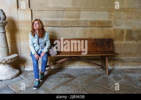 Frau, die auf einer alten Holzbank sitzt und leise wartet. Stockfoto