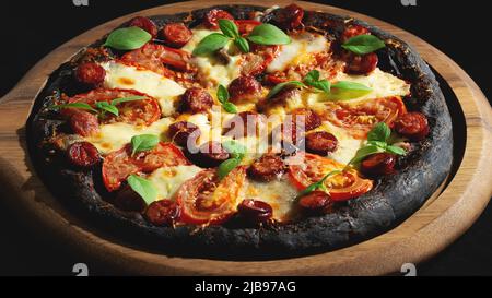 Schwarze Pizza mit Tomaten, Würstchen, Mozzarella und Basilikum. Teig mit gesundem Bambuskohlepulver Stockfoto