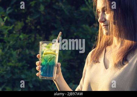 Eine junge Frau mit langen dunklen Haaren hält einen erfrischenden Cocktail in der Hand. Selektiver Fokus Stockfoto